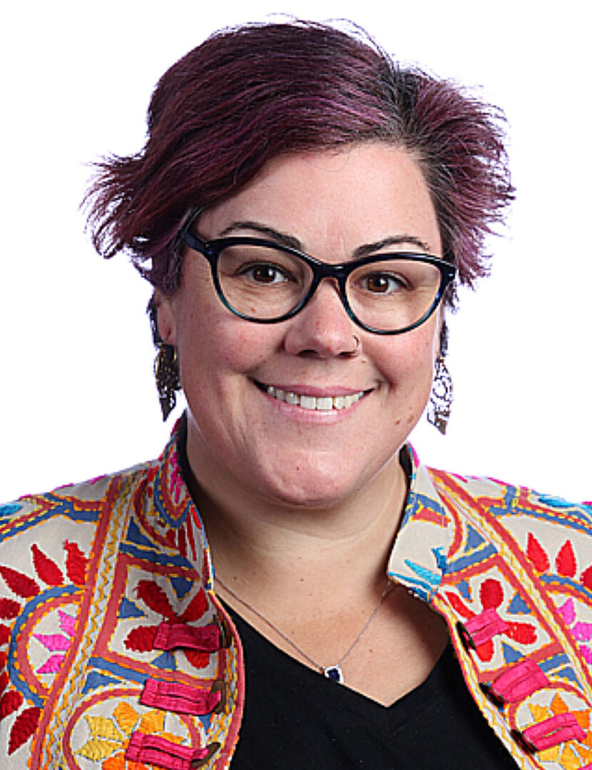 A woman with purple hair and glasses smiling.